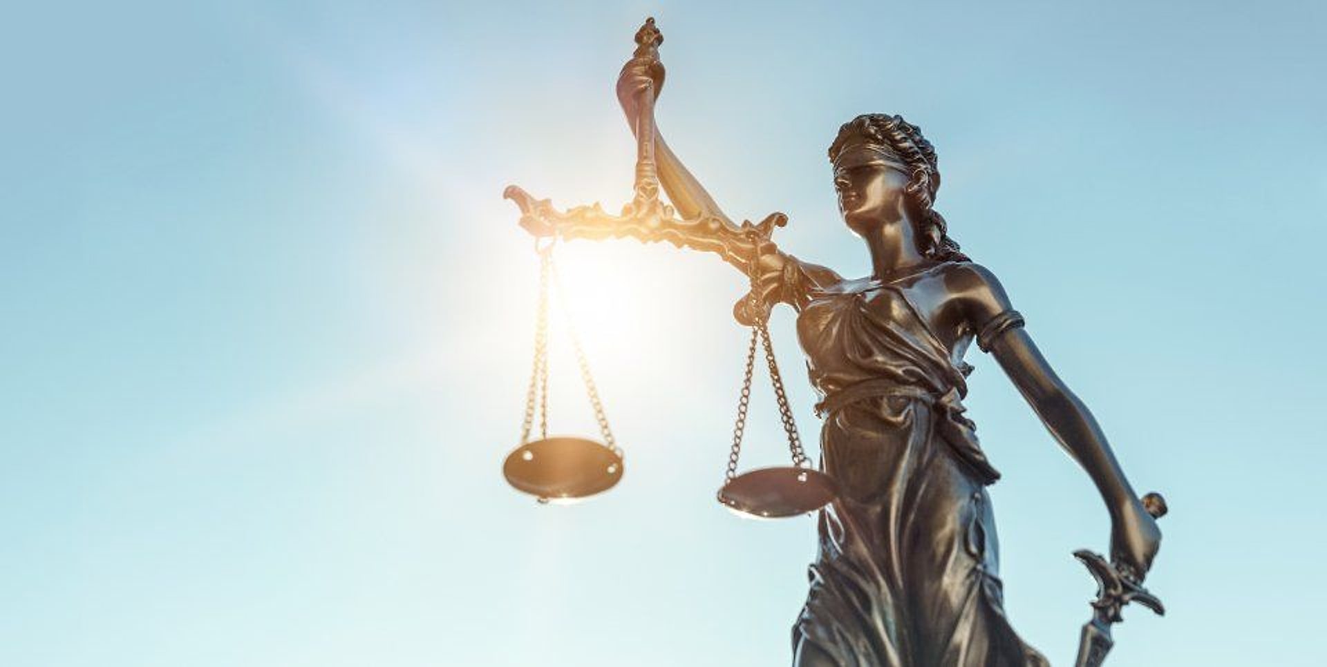 Statua della Giustizia bendata che regge la bilancia, in controluce contro il cielo.